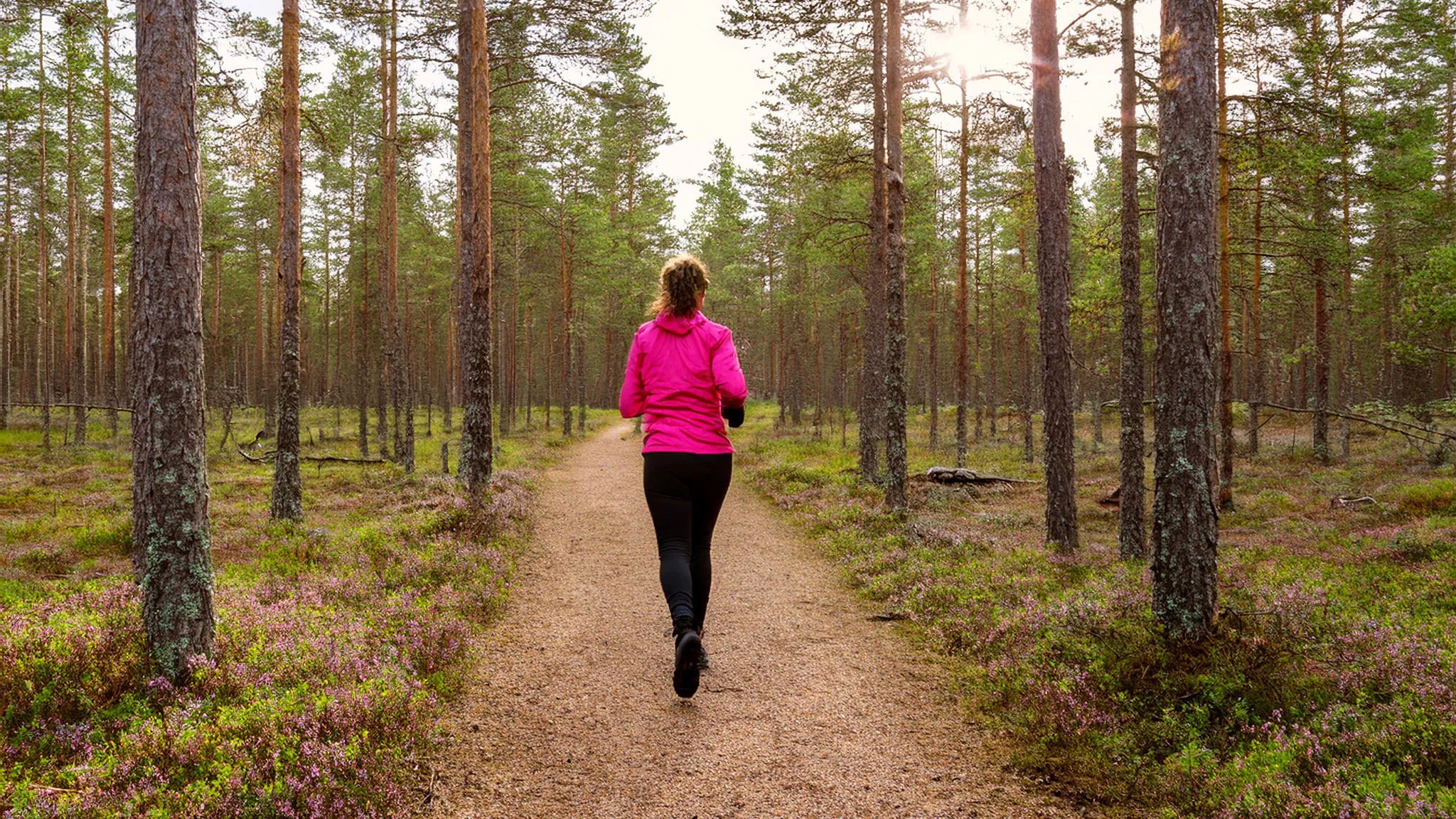 Nainen juoksee kuntopolulla kangasmaastossa.